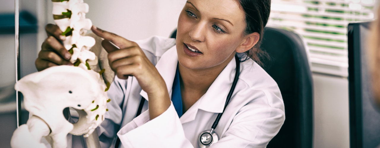 Female physical therapist pointing at a model of vertebrae to indicate pain point.